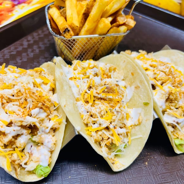 Three soft tacos filled with meat, cheese, and sauce, alongside a basket of golden fries.