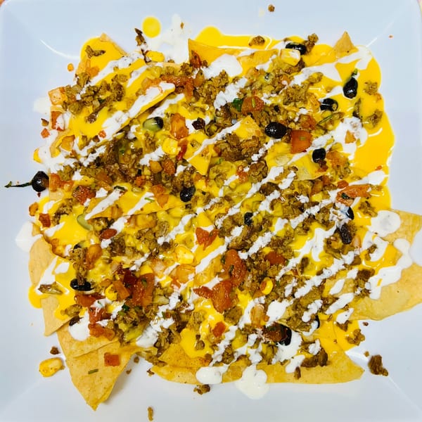 A plate of Carytown Gyro's Mediterranean nachos, topped with meat, cheese, black olives, and white sauce.