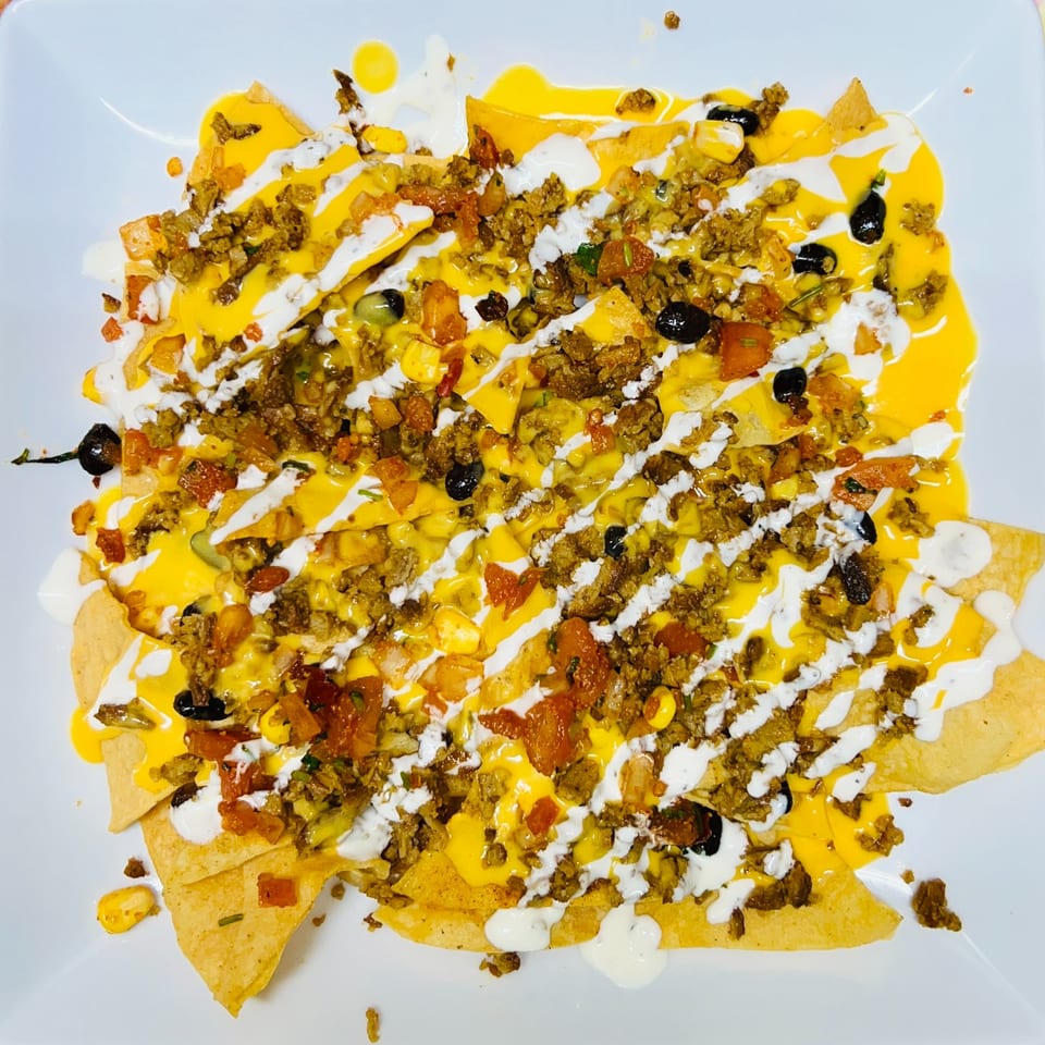A plate of Carytown Gyro's Mediterranean nachos, topped with meat, cheese, black olives, and white sauce.
